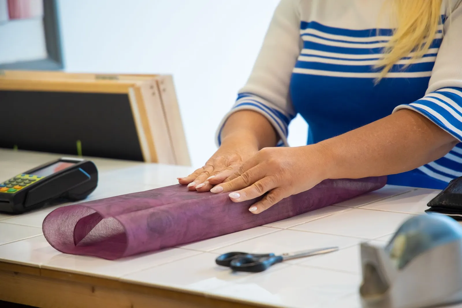 Des mains emballent un objet dans du papier, sur le comptoir d’une boutique